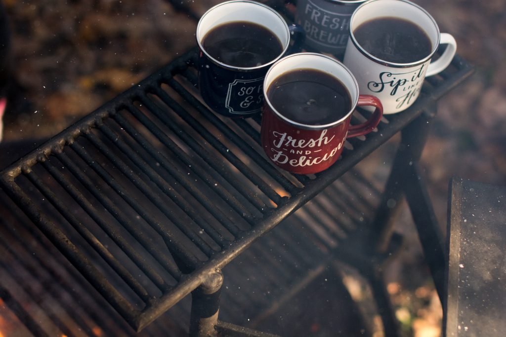 four mugs of coffee on a campfire grate